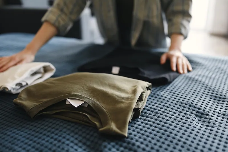 Unas manos ordenan camisetas dobladas sobre una cama.