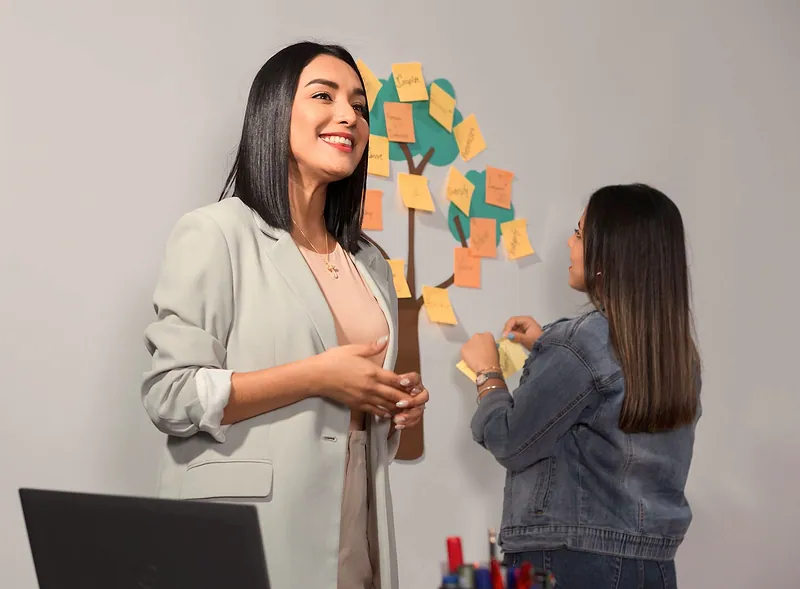 Una facilitadora guía una sesión de trabajo con notas adhesivas en la pared.