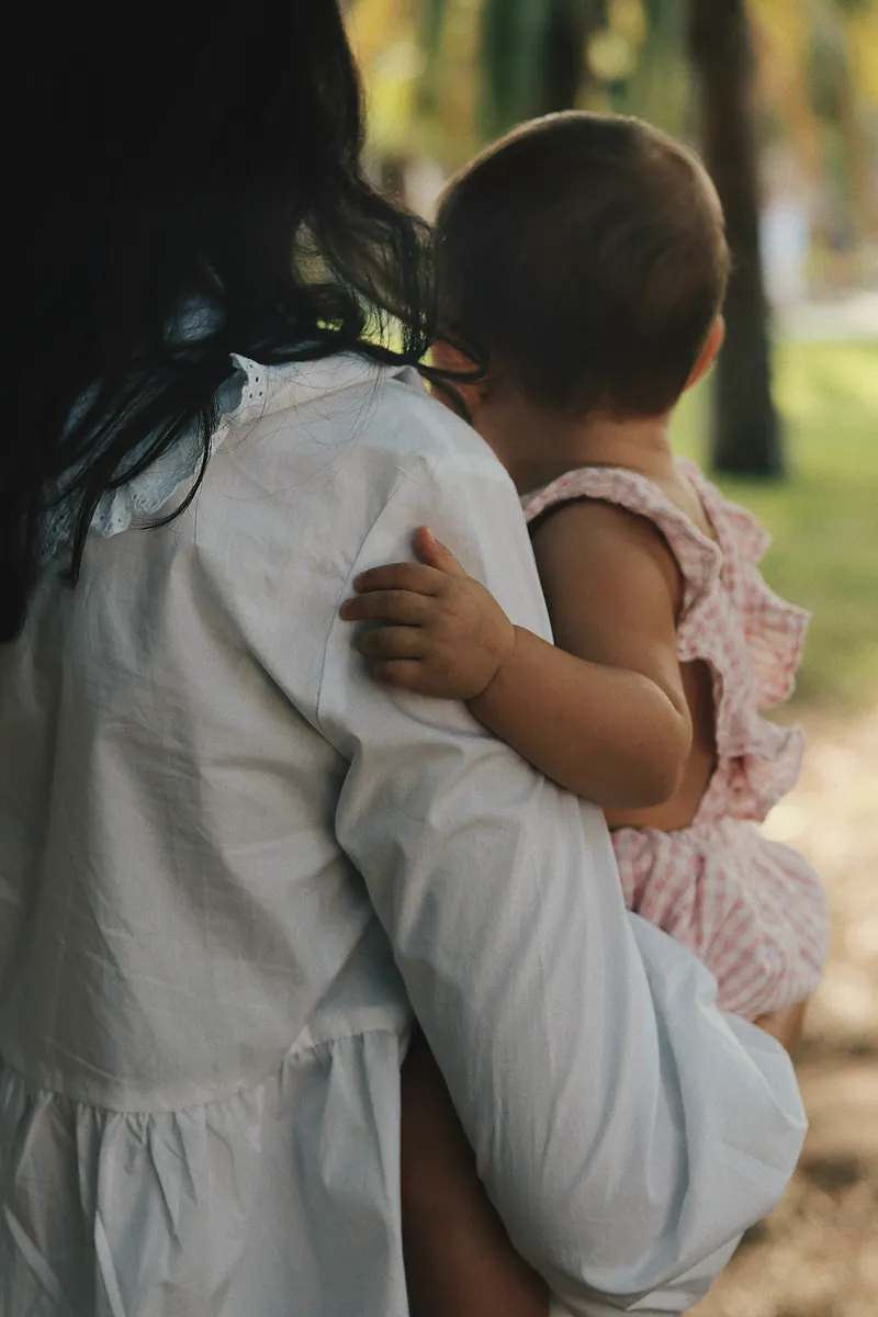 Una mujer carga a una bebé en brazos; las dos están de espaldas.
